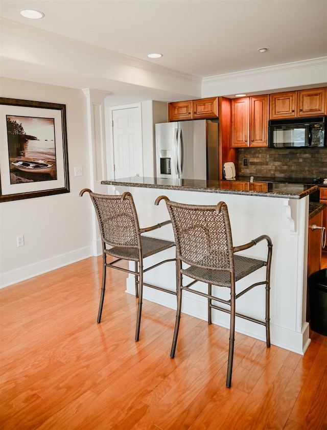 706 N Dockside Cir, Suttons Bay, MI 49682 - kitchen with black microwave, stainless steel fridge with ice dispenser, a breakfast bar, brown cabinets, and light wood-type flooring