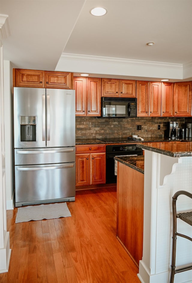 706 N Dockside Cir, Suttons Bay, MI 49682 - kitchen with black appliances, light wood-type flooring, dark stone counters, brown cabinetry, and decorative backsplash