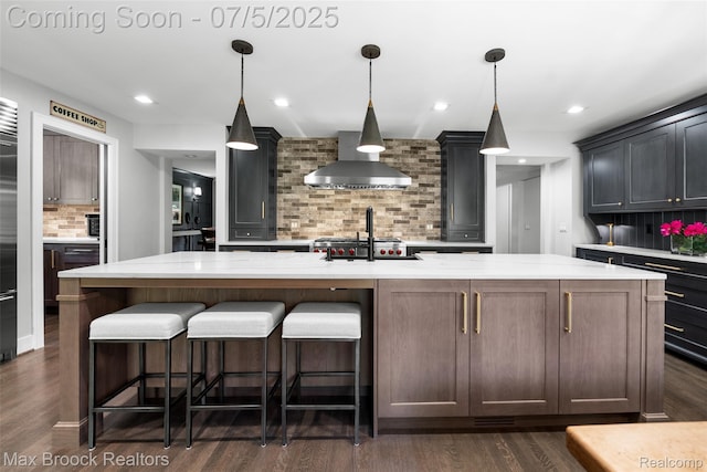 6907 W Knollwood Cir W, Bloomfield, MI 48322 - kitchen featuring wall chimney range hood, decorative backsplash, dark wood-style floors, an island with sink, and light stone counters