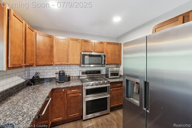 4577 Oaklawn Dr, Pinckney, MI 48169 - kitchen with stainless steel appliances, dark wood finished floors, tasteful backsplash, brown cabinetry, and dark stone counters
