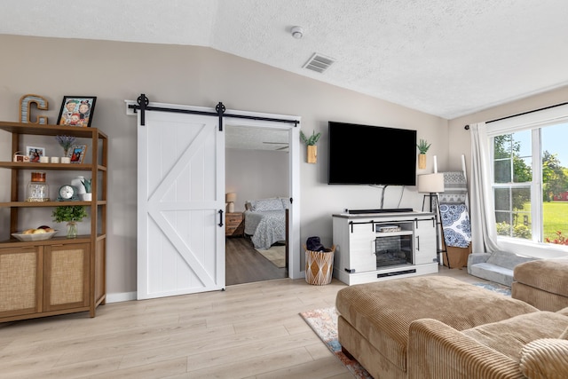 7241 Cherry Ave, Kewadin, MI 49648 - living area with vaulted ceiling, a barn door, light wood-style flooring, and a textured ceiling