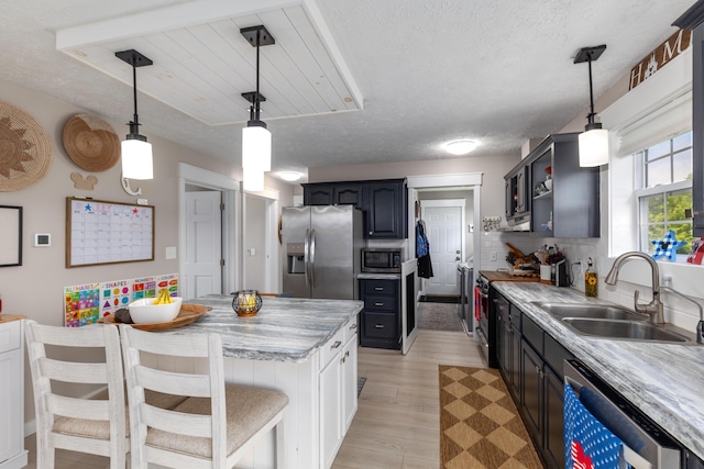 7241 Cherry Ave, Kewadin, MI 49648 - kitchen featuring stainless steel appliances, light wood finished floors, a textured ceiling, pendant lighting, and a breakfast bar area