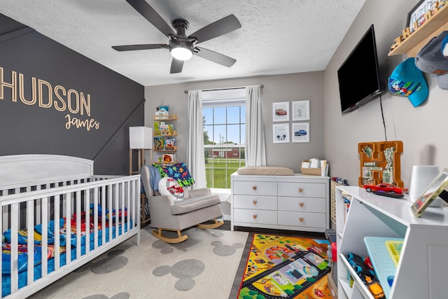 7241 Cherry Ave, Kewadin, MI 49648 - bedroom with a textured ceiling, a nursery area, a ceiling fan, and wood finished floors