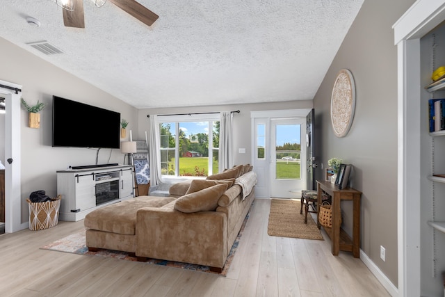 7241 Cherry Ave, Kewadin, MI 49648 - living room featuring a ceiling fan, light wood-style floors, a textured ceiling, and vaulted ceiling