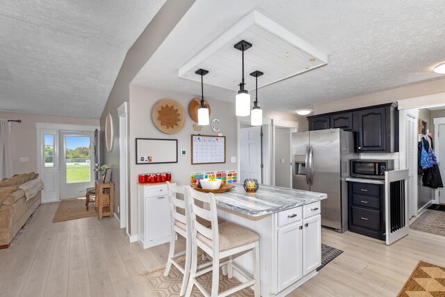 7241 Cherry Ave, Kewadin, MI 49648 - kitchen with appliances with stainless steel finishes, a textured ceiling, light wood-style flooring, a kitchen bar, and a center island