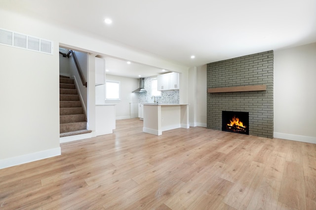 20157 Huntington Ave, Harper Woods, MI 48225 - unfurnished living room featuring light wood-type flooring, a brick fireplace, stairs, and recessed lighting