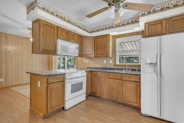 1196 S Dettman Rd, Jackson, MI 49203 - kitchen featuring white appliances, dark countertops, ceiling fan, light wood-style floors, and wood walls
