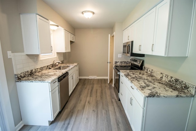 3745 Holly Ave, Flint, MI 48506 - kitchen featuring appliances with stainless steel finishes, light wood-style floors, tasteful backsplash, light stone countertops, and white cabinetry
