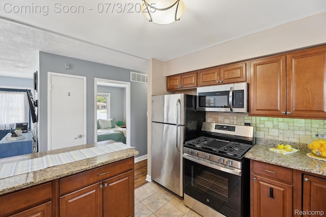 29934 Tamarack Dr, Gibraltar, MI 48134 - kitchen with stainless steel appliances, tasteful backsplash, light stone counters, and brown cabinetry