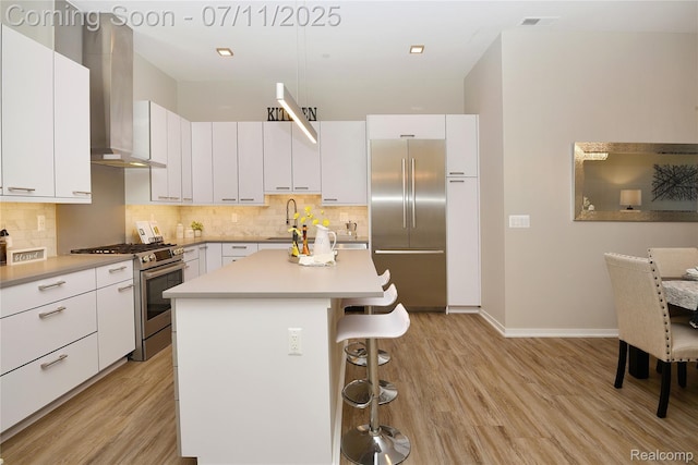 750 Forest Ave Unit 202, Birmingham, MI 48009 - kitchen with appliances with stainless steel finishes, wall chimney exhaust hood, a kitchen bar, light wood finished floors, and backsplash