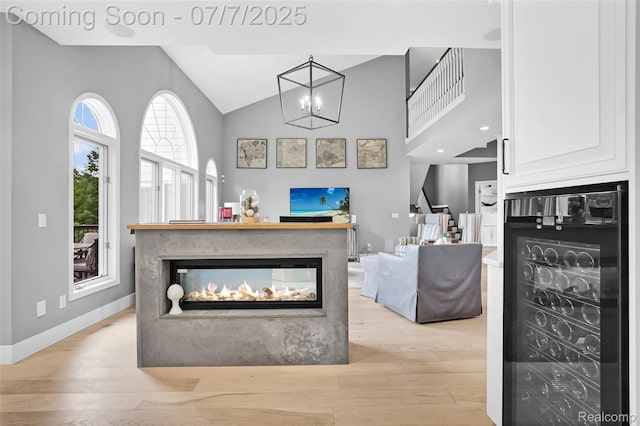 2545 Hartun Dr, Brighton, MI 48114 - living room with beverage cooler, light wood finished floors, stairs, a multi sided fireplace, and high vaulted ceiling