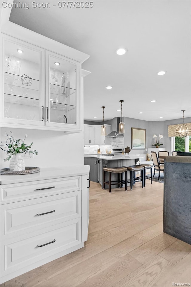 2545 Hartun Dr, Brighton, MI 48114 - kitchen featuring wall chimney exhaust hood, light wood-style floors, light countertops, white cabinets, and recessed lighting