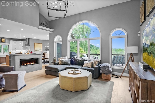 2545 Hartun Dr, Brighton, MI 48114 - living area featuring a high ceiling, light wood-style floors, a lit fireplace, a chandelier, and recessed lighting