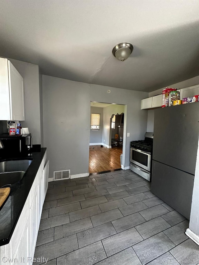 16595 Griggs St, Detroit, MI 48221 - kitchen with stainless steel range with gas cooktop, freestanding refrigerator, wood tiled floors, white cabinets, and dark countertops