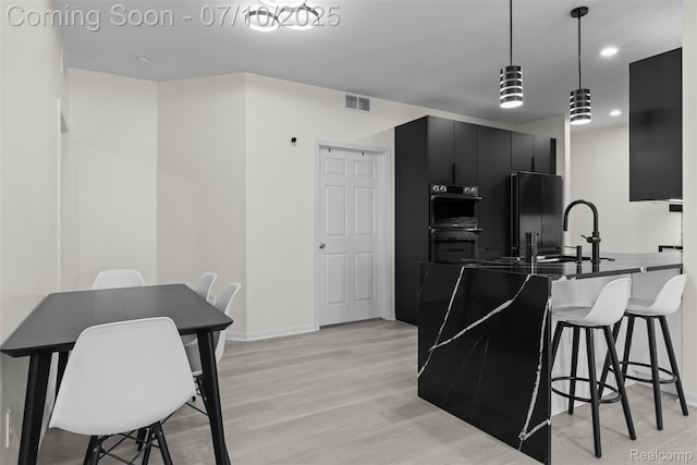 8461 Towne Center Cir N, Warren, MI 48093 - kitchen with dark cabinets, black refrigerator, double wall oven, a breakfast bar area, and light wood-style flooring