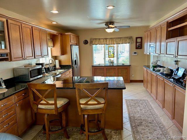 32241 N River Rd, Harrison Township, MI 48045 - kitchen with stainless steel appliances, ceiling fan, brown cabinets, a peninsula, and dark countertops