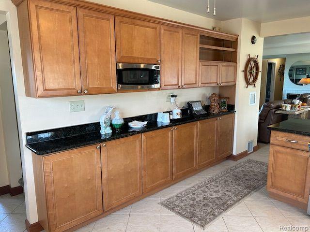 32241 N River Rd, Harrison Township, MI 48045 - kitchen featuring stainless steel microwave, open shelves, brown cabinets, light tile patterned flooring, and dark stone countertops