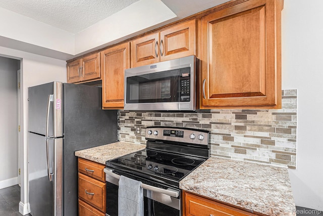 8150 24 Mile Rd, Shelby Twp, MI 48316 - kitchen with appliances with stainless steel finishes, brown cabinetry, a textured ceiling, tasteful backsplash, and light stone counters