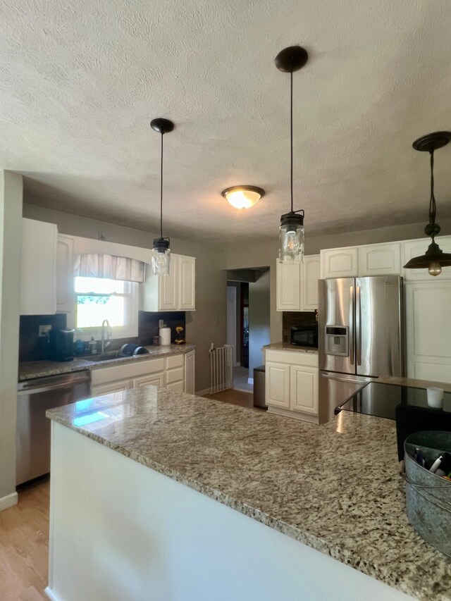 7220 W 64th St, Fremont, MI 49412 - kitchen with appliances with stainless steel finishes, white cabinets, light stone countertops, a textured ceiling, and pendant lighting