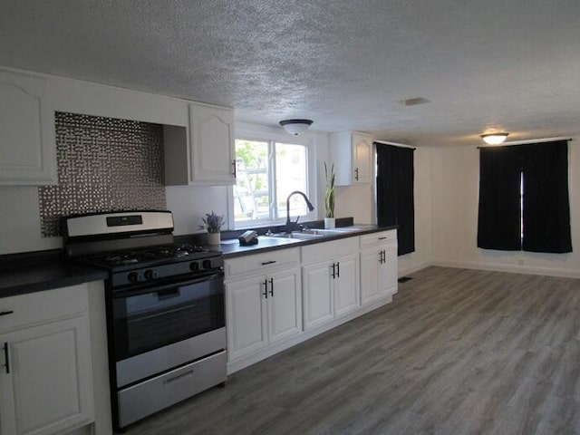 168 Fremont St, Bronson, MI 49028 - kitchen featuring stainless steel gas range oven, dark countertops, wood finished floors, white cabinetry, and a textured ceiling