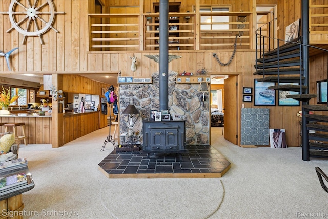 8641 Brettonwood Shores Rd, Rapid City, MI 49676 - living area featuring wooden walls, carpet floors, a towering ceiling, stairway, and a wood stove