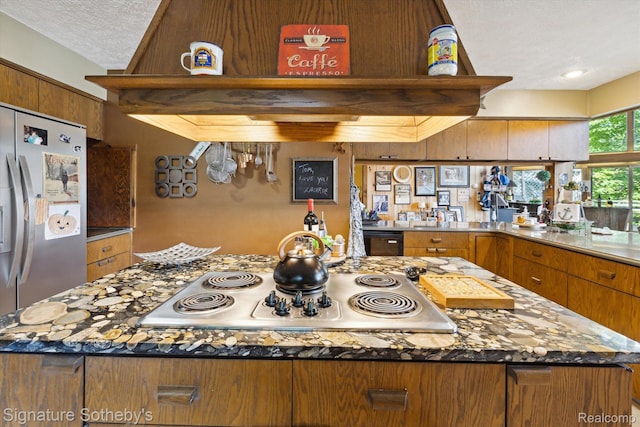 8641 Brettonwood Shores Rd, Rapid City, MI 49676 - kitchen with stainless steel appliances, a kitchen island, brown cabinetry, a textured ceiling, and stone countertops
