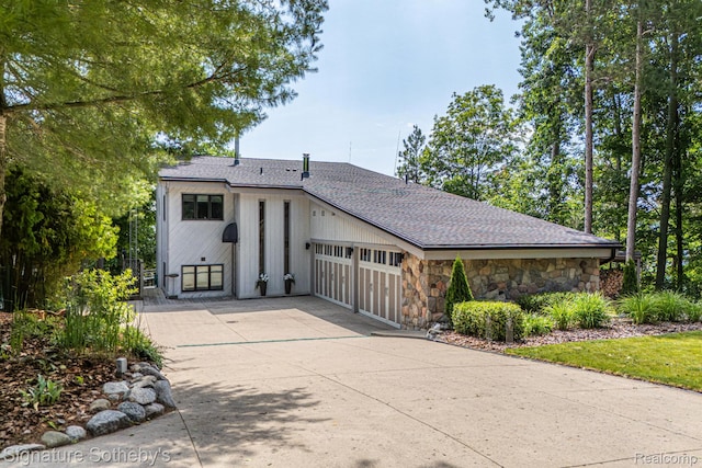 8641 Brettonwood Shores Rd, Rapid City, MI 49676 - view of front of house with stone siding, a garage, concrete driveway, and a shingled roof