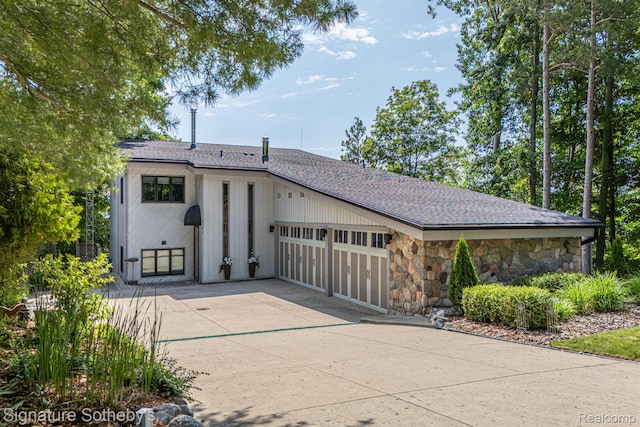 8641 Brettonwood Shores Rd, Rapid City, MI 49676 - view of front of property with stone siding, a garage, driveway, and roof with shingles