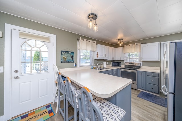 19336 E Chippewa Dr, Chippewa Lake, MI 49320 - kitchen with stainless steel appliances, a peninsula, a kitchen bar, light wood-type flooring, and light countertops