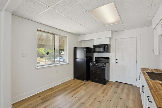 400 Burton St SW, Grand Rapids, MI 49507 - kitchen with butcher block counters, black appliances, light wood-type flooring, a paneled ceiling, and white cabinets