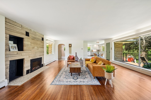 3017 Niles Buchanan Rd, Buchanan, MI 49107 - living area featuring a baseboard radiator, a stone fireplace, arched walkways, and wood finished floors