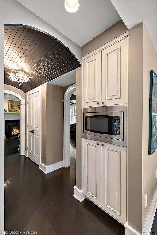 504 Landon St, Birmingham, MI 48009 - kitchen featuring stainless steel microwave, arched walkways, dark wood-style floors, a warm lit fireplace, and white cabinetry