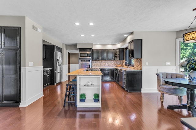 3800 Guest Rd, Jackson, MI 49203 - kitchen with appliances with stainless steel finishes, open shelves, a kitchen island, wainscoting, and light stone counters