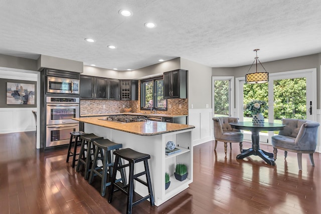 3800 Guest Rd, Jackson, MI 49203 - kitchen with stainless steel appliances, a breakfast bar area, a textured ceiling, dark wood finished floors, and tasteful backsplash