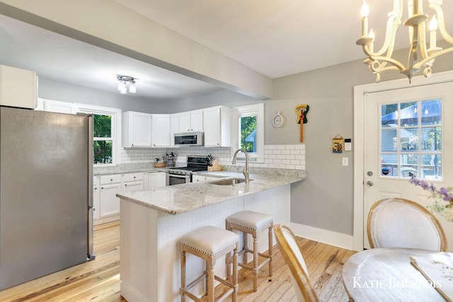 140 S Monroe St NE, Rockford, MI 49341 - kitchen with appliances with stainless steel finishes, light wood finished floors, a peninsula, light stone counters, and tasteful backsplash