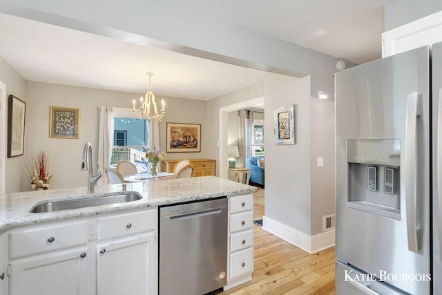 140 S Monroe St NE, Rockford, MI 49341 - kitchen featuring appliances with stainless steel finishes, light wood-style flooring, a chandelier, white cabinetry, and light stone counters