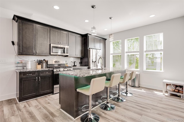 5973 Stella, Troy, MI 48085 - kitchen with appliances with stainless steel finishes, a kitchen bar, light wood-type flooring, backsplash, and an island with sink
