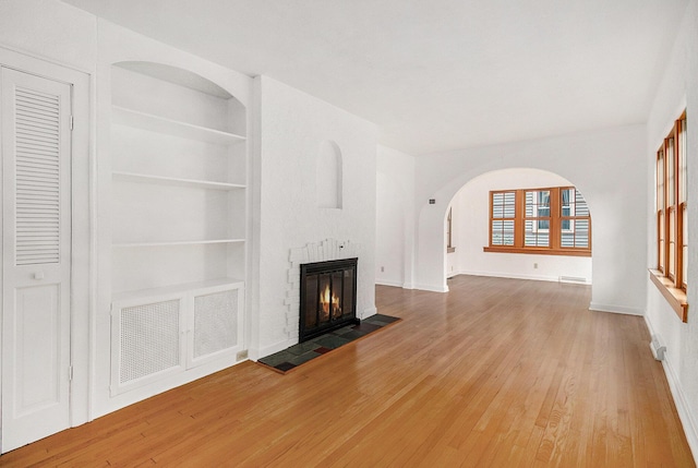 838 Lakeway Ave, Kalamazoo, MI 49001 - unfurnished living room with arched walkways, built in shelves, wood finished floors, and a glass covered fireplace