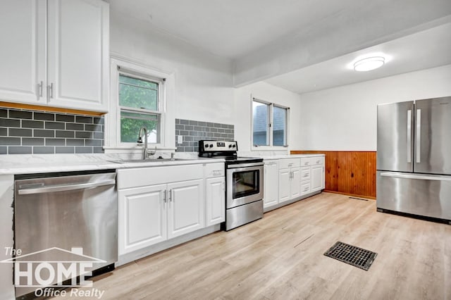 1114 Lynn St, Owosso, MI 48867 - kitchen with stainless steel appliances, light wood-type flooring, white cabinetry, a wainscoted wall, and tasteful backsplash