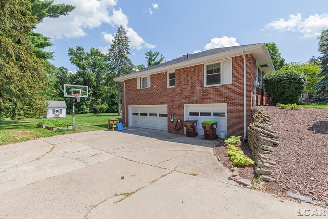 144 N Scott St, Adrian, MI 49221 - view of side of property featuring a garage, driveway, brick siding, and a lawn