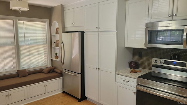 401 Budlong St, Adrian, MI 49221 - kitchen with appliances with stainless steel finishes, white cabinetry, light wood-style floors, decorative backsplash, and light stone counters