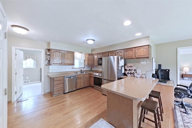 9100 Mayfred Dr, Pinckney, MI 48169 - kitchen with stainless steel appliances, a peninsula, a kitchen breakfast bar, light wood-style flooring, and light countertops