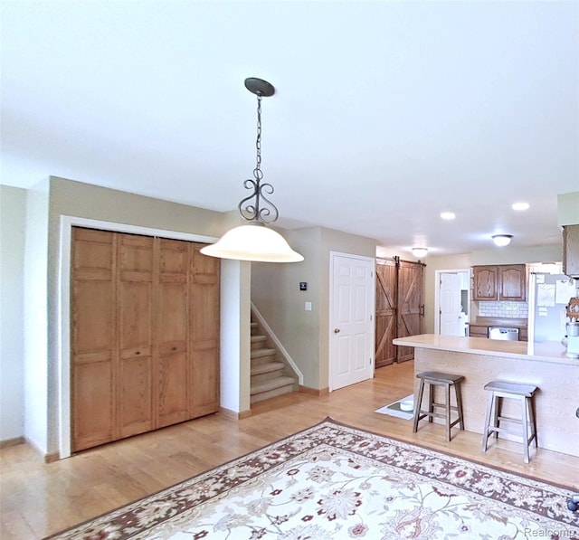 9100 Mayfred Dr, Pinckney, MI 48169 - kitchen featuring a barn door, light wood finished floors, a kitchen breakfast bar, stainless steel dishwasher, and a peninsula