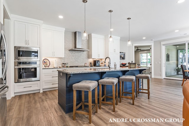 2063 Ottawa Beach Rd, Holland, MI 49424 - kitchen featuring appliances with stainless steel finishes, wall chimney exhaust hood, light wood-style floors, decorative backsplash, and an island with sink