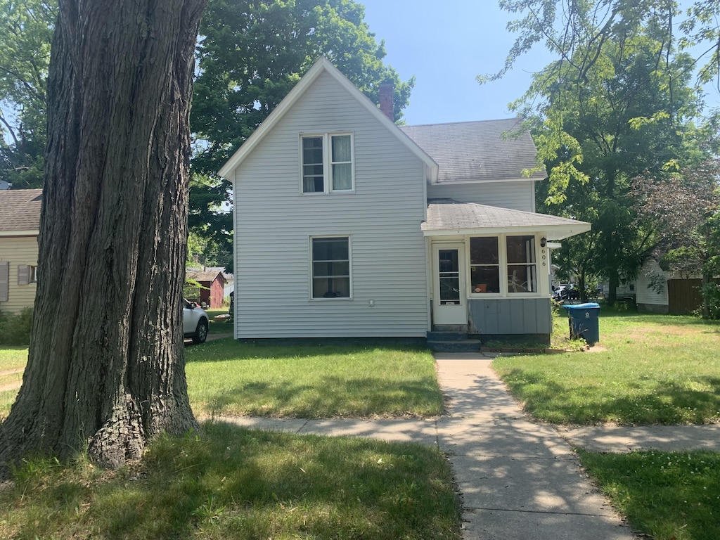 606 N Harrison St, Ludington, MI 49431 - traditional home with a front yard, entry steps, roof with shingles, and a chimney