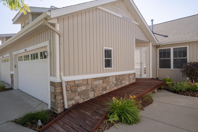 10068 S Crossroads Cir SE, Caledonia, MI 49316 - view of side of home with stone siding, an attached garage, board and batten siding, concrete driveway, and roof with shingles