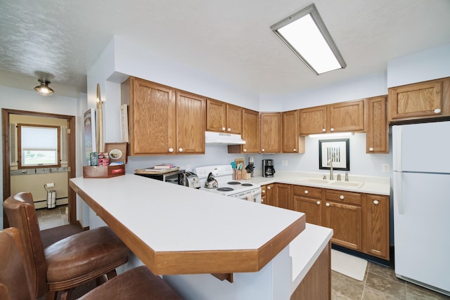 5015 Main St, Onekama, MI 49675 - kitchen featuring white appliances, under cabinet range hood, a baseboard radiator, and brown cabinetry