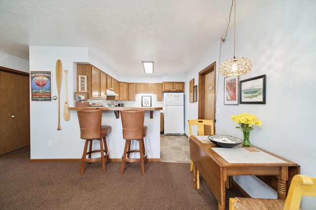 5015 Main St, Onekama, MI 49675 - kitchen featuring freestanding refrigerator, a peninsula, a breakfast bar area, light carpet, and hanging light fixtures