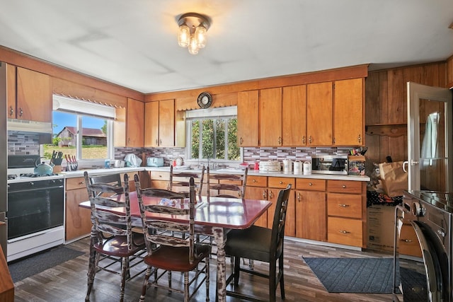8698 Big Stone Lake Rd, Evart, MI 49631 - kitchen featuring white range with gas stovetop, stainless steel microwave, brown cabinets, backsplash, and wood walls