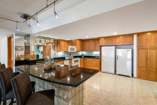 15665 Portage Rd, Vicksburg, MI 49097 - kitchen with white appliances, brown cabinetry, dark stone counters, recessed lighting, and a peninsula